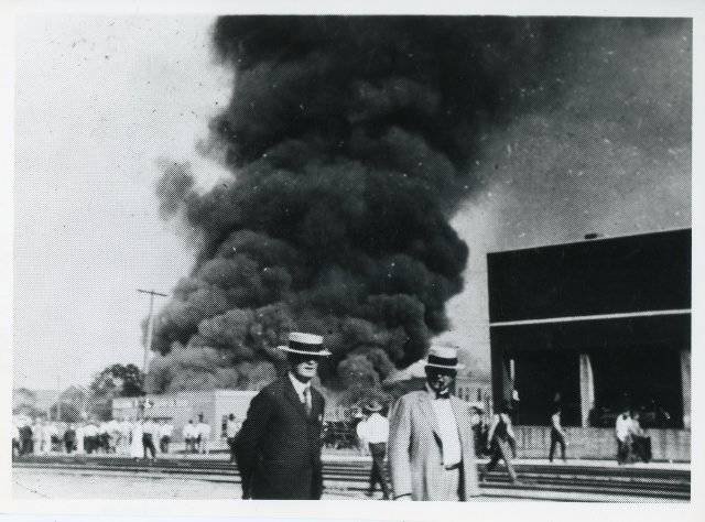 Two white men talks as Black Wall Street burns behind them. Tulsa Race Massacre 